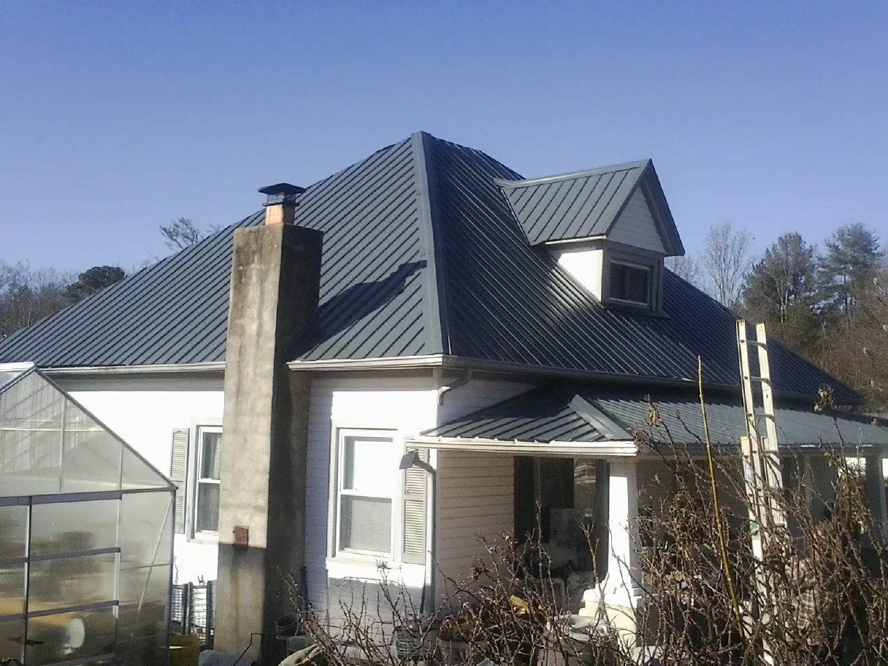 Dark blue standing seam metal roof on a white farmhouse with dormer — Slate & Tile Roof Repair by Roofing Brothers in Springdale