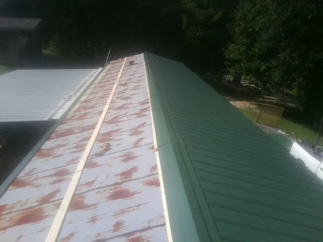 Old rusted panels beside newly installed green metal roofing — Wind Damage Roof Repair by Roofing Brothers in Springdale