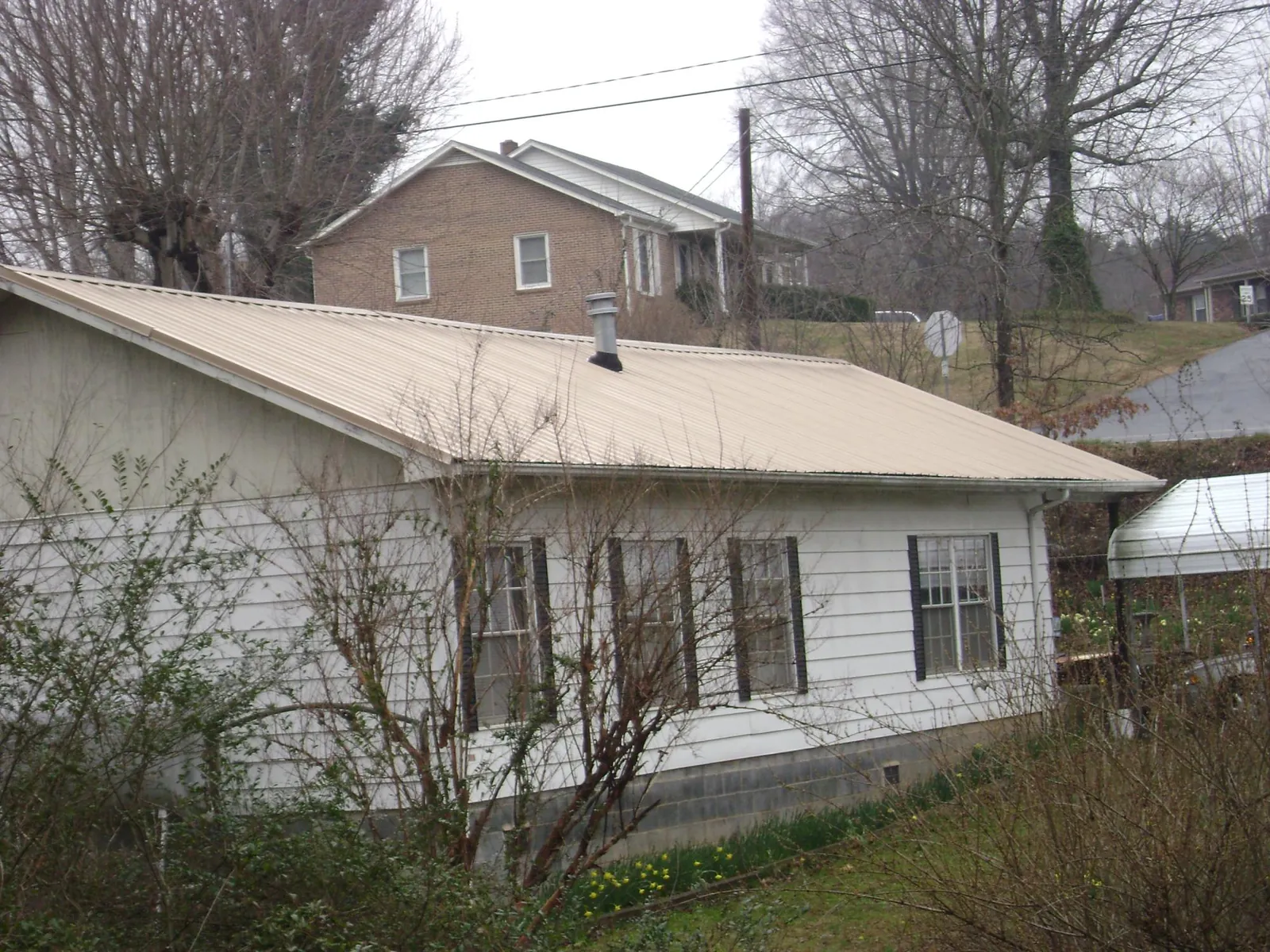 Tan metal roof on a white sided house set into a hillside — Commercial Roofing by Roofing Brothers in Springdale